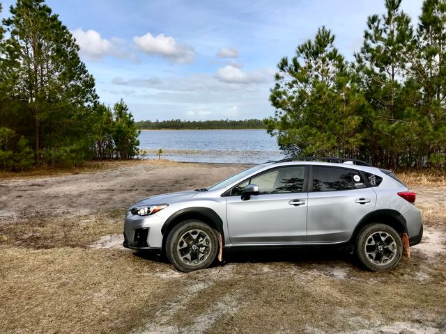 A silver SUV parked near a tranquil lake, surrounded by trees and nature.